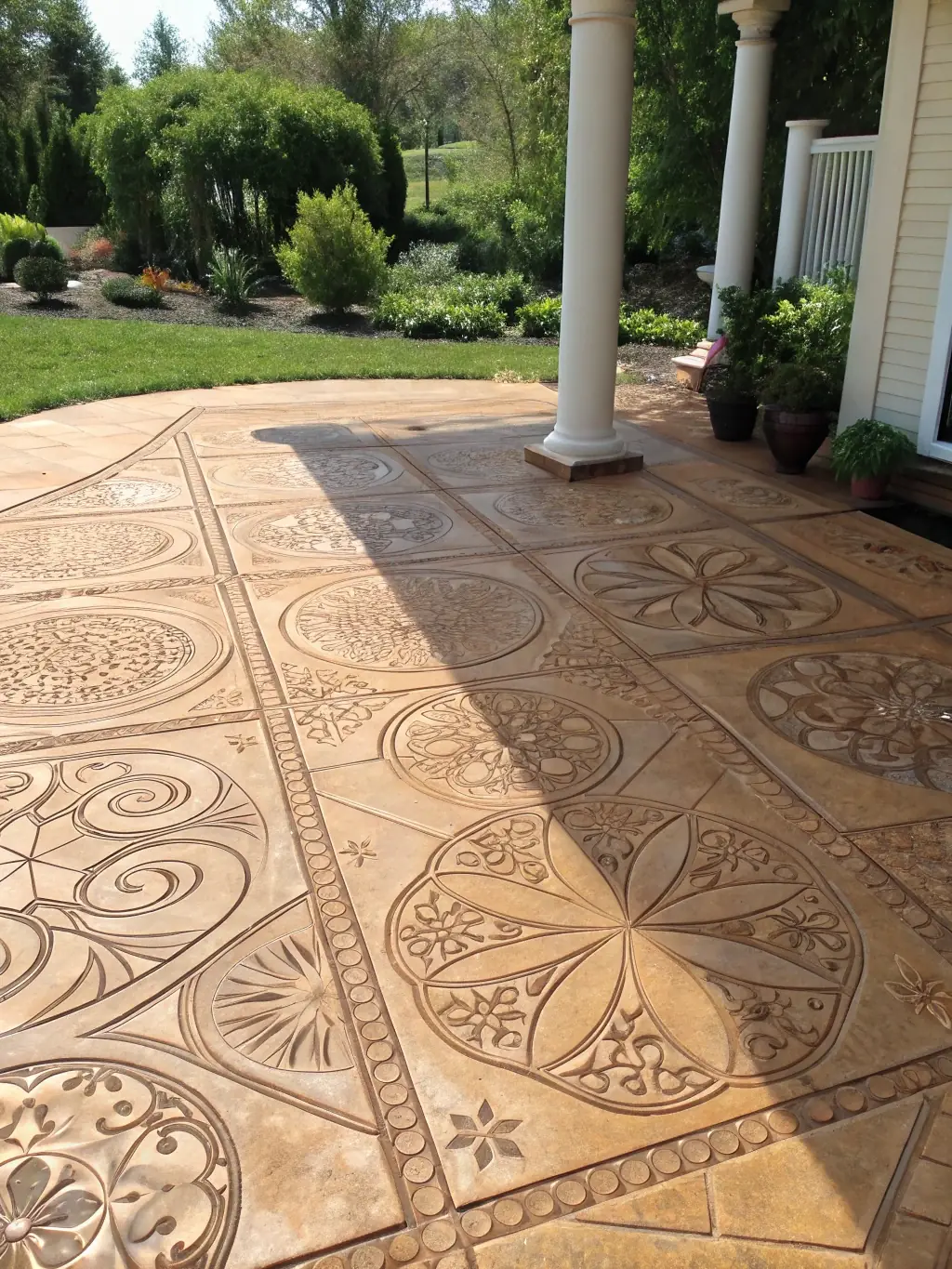 A close-up shot of a stamped concrete patio with a complex, decorative pattern resembling natural stone. The patio includes an outdoor kitchen area with a built-in grill and bar.